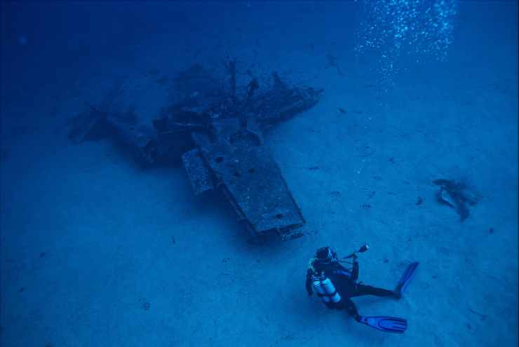 photo of person scuba diving near wreckage